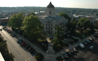 Aerial view of the Monroe County Courthouse in downtown Bloomington, Indiana, surrounded by tree-lined streets, historic buildings, and parked cars.