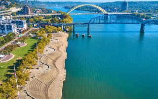 Aerial view of Cincinnati, Ohio, featuring the riverfront park and bridges spanning the Ohio River on a clear, sunny day.
