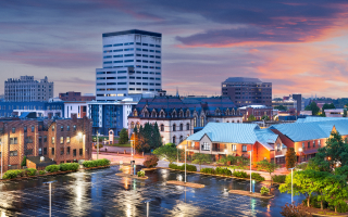 Alt Text Downtown Evansville, Indiana skyline at sunset with city buildings, streets, and wet pavement.