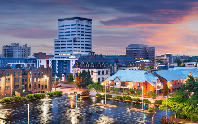 Alt Text Downtown Evansville, Indiana skyline at sunset with city buildings, streets, and wet pavement.