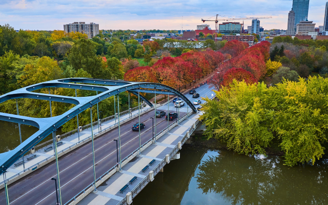Aerial view of a bridge over the river with the Fort Wayne, Indiana skyline and colorful fall foliage in the background.