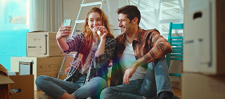 A young couple who have just bought a house and video call their friends or family on their phone to show them the key of the new house.