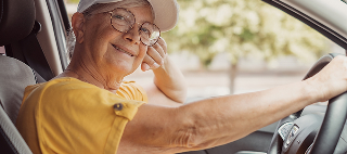 Portrait of a relaxed senior woman holding the car steering wheel, looking at the camera.
